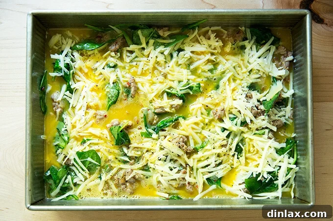 A 9x13-inch baking pan, generously filled with a harmonious blend of eggs, cheese, sausage, spinach, and onions, all ready for the oven.
