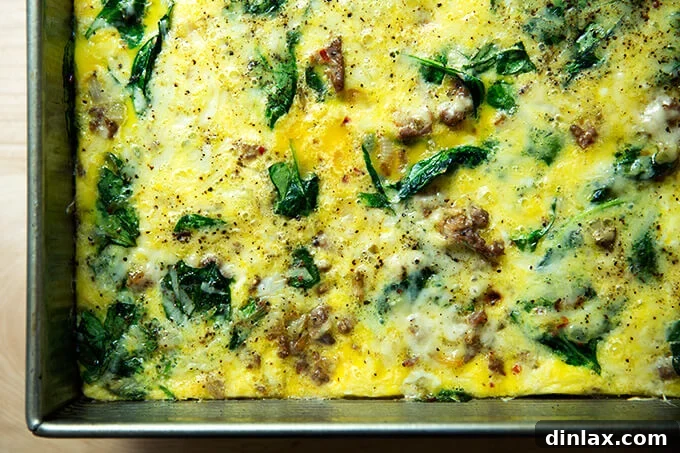 A beautifully baked breakfast casserole, exhibiting a golden crust and a delightful blend of visible eggs, Gruyère cheese, sausage, spinach, and caramelized onions.