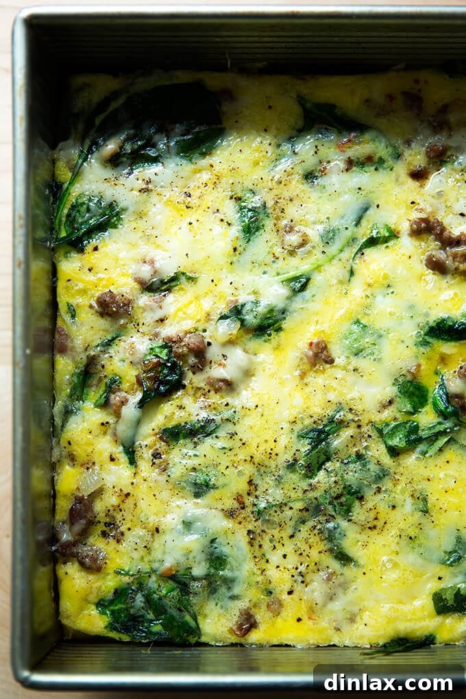 An inviting up-close shot of a warm, perfectly cooked slice of the breakfast casserole, revealing its rich layers of eggs, Gruyère cheese, sausage, spinach, and onions.