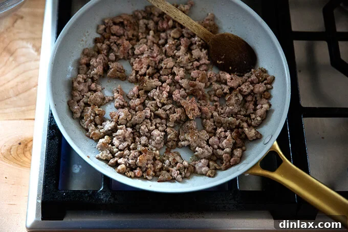 Hot Italian sausage browning in a pan on the stovetop, releasing savory aromas.