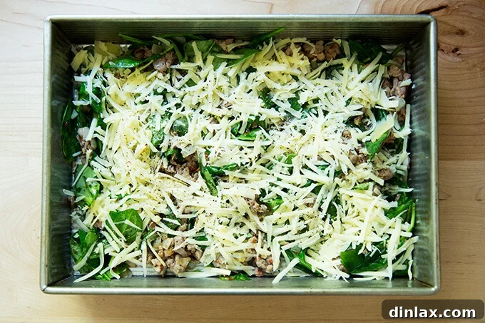 A 9x13-inch baking pan beautifully filled with layers of savory sausage, fresh spinach, sweet caramelized onions, and generous amounts of grated cheese.