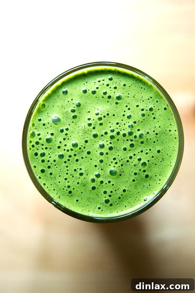 Overhead shot of vibrant vegan green smoothie with almond milk, banana, and spinach, garnished with mint.