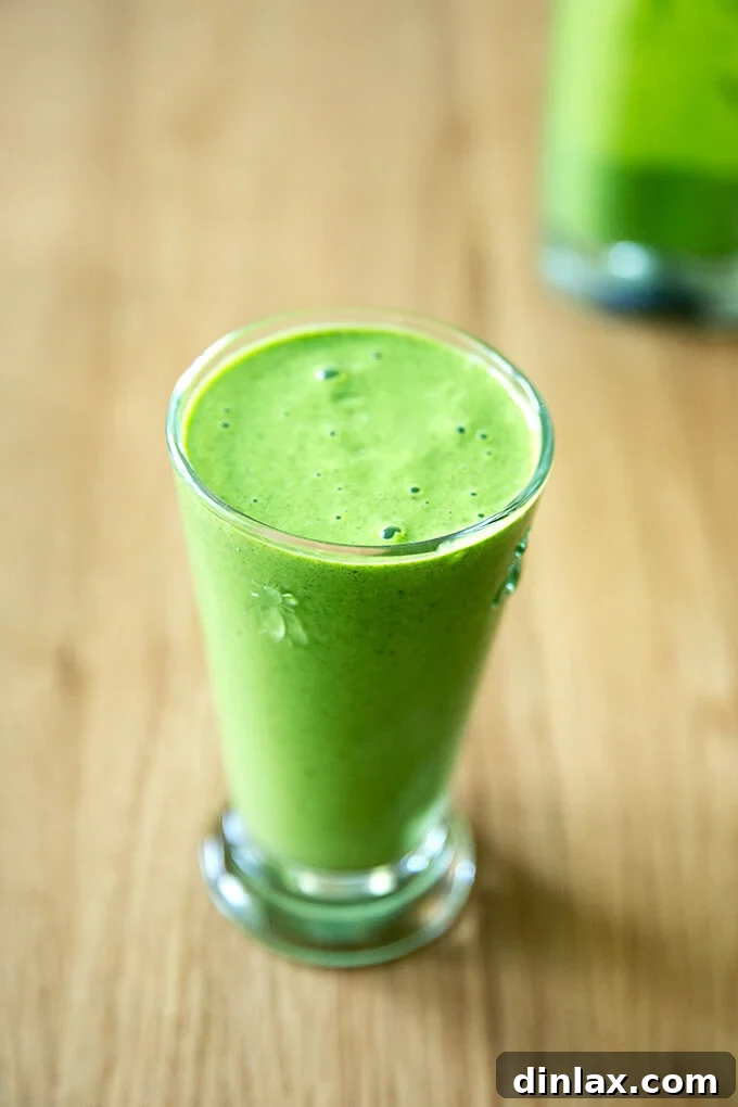 A tall glass filled with a vibrant green smoothie, garnished with a single spinach leaf.