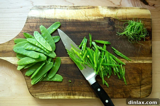 Vibrant Spring Fattoush 9 Crisp slivered snow peas arranged on a cutting board next to a chef's knife, prepped and ready for addition to the spring salad.