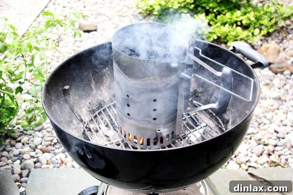 A charcoal Weber grill with a chimney starter holding burning coals inside, ready for grilling.