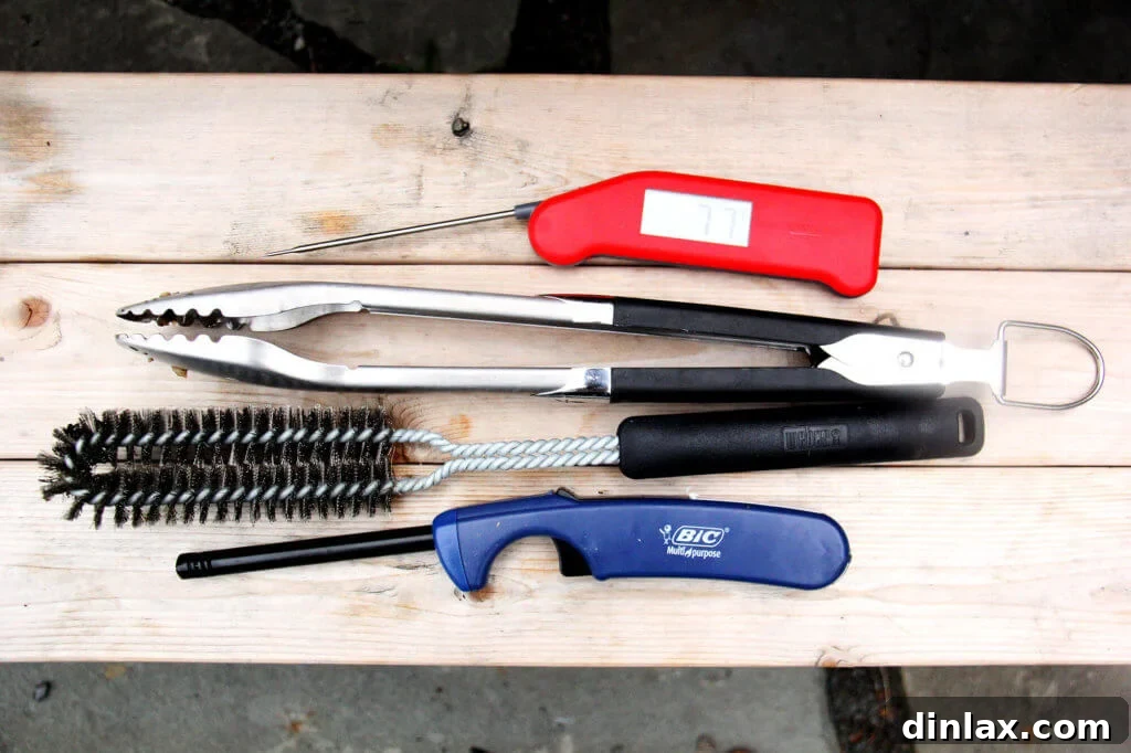 Assortment of grilling tools including long tongs, a lighter, grill brush, and heat-resistant gloves.