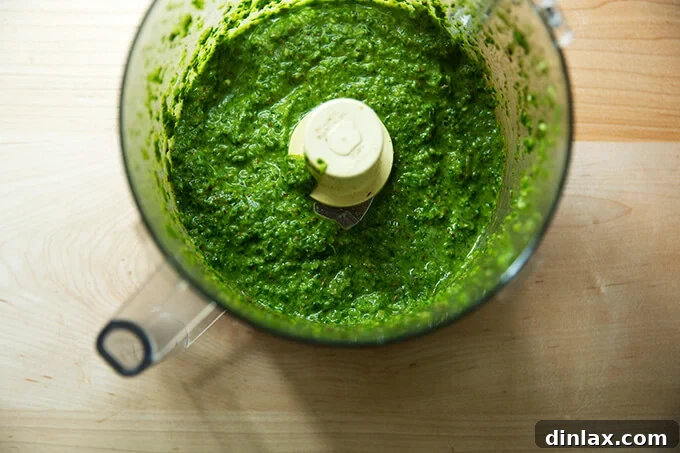 A food processor brimming with vibrant green skhug, an aromatic blend of parsley, cilantro, cumin, coriander, garlic, jalapenos, olive oil, and lemon.