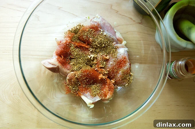 Raw chicken thighs coated with a vibrant blend of salt, smoked paprika, toasted cumin, and coriander, ready for marination.