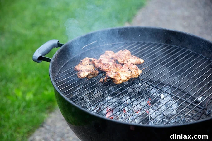 Close-up view of boneless chicken thighs sizzling and charring on a hot grill grate, illustrating the quick cooking process for perfectly grilled chicken.