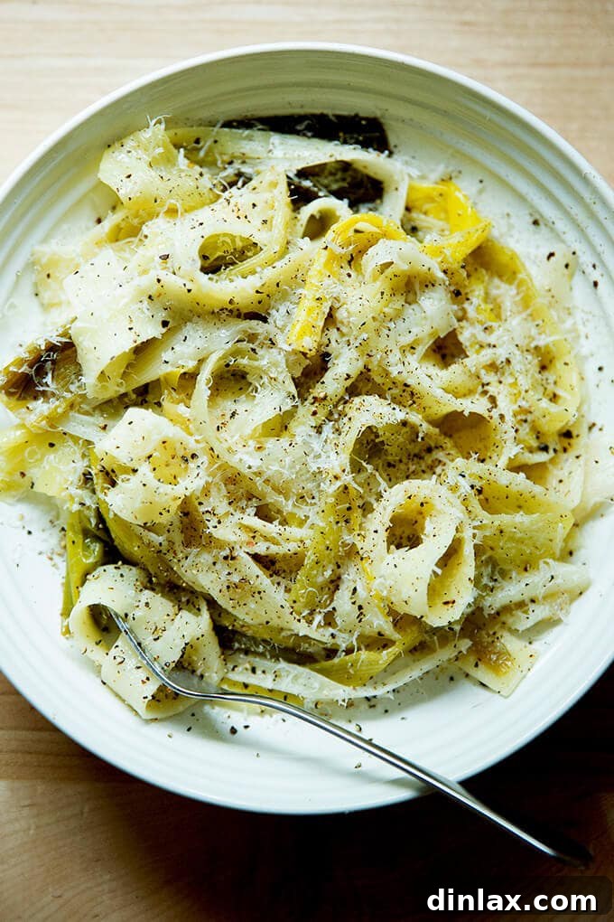 A bowl of braised leek pappardelle with a fork and grated parmesan over top, ready to be enjoyed.