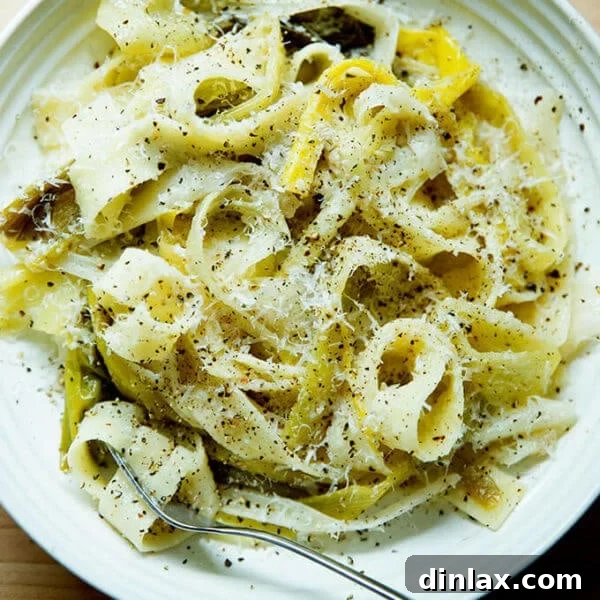 A bowl of braised leek pappardelle with a fork and grated parmesan over top.