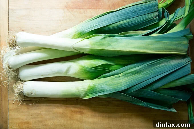 Fresh, whole leeks displayed on a rustic wooden cutting board, ready for preparation.