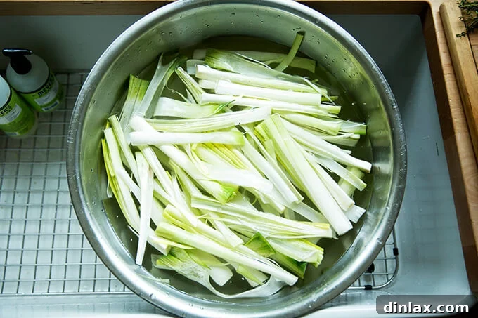 A large, clear bowl filled with sliced leeks soaking in clean water to remove any hidden dirt or grit.