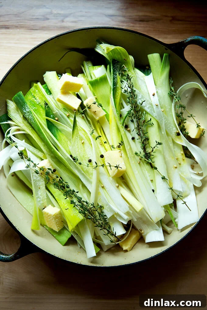 A braising pan containing carefully arranged leeks, infused with olive oil, butter, white wine, water, and aromatic herbs, poised for braising.