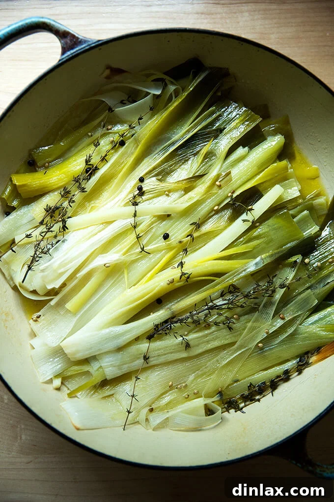 Just-braised leeks, golden and tender, glistening in their fragrant broth within a braising pan.