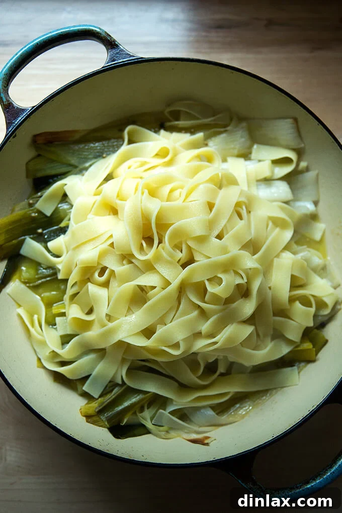 A braising pan generously filled with tender braised leeks and freshly cooked pappardelle pasta, gently tossed together.