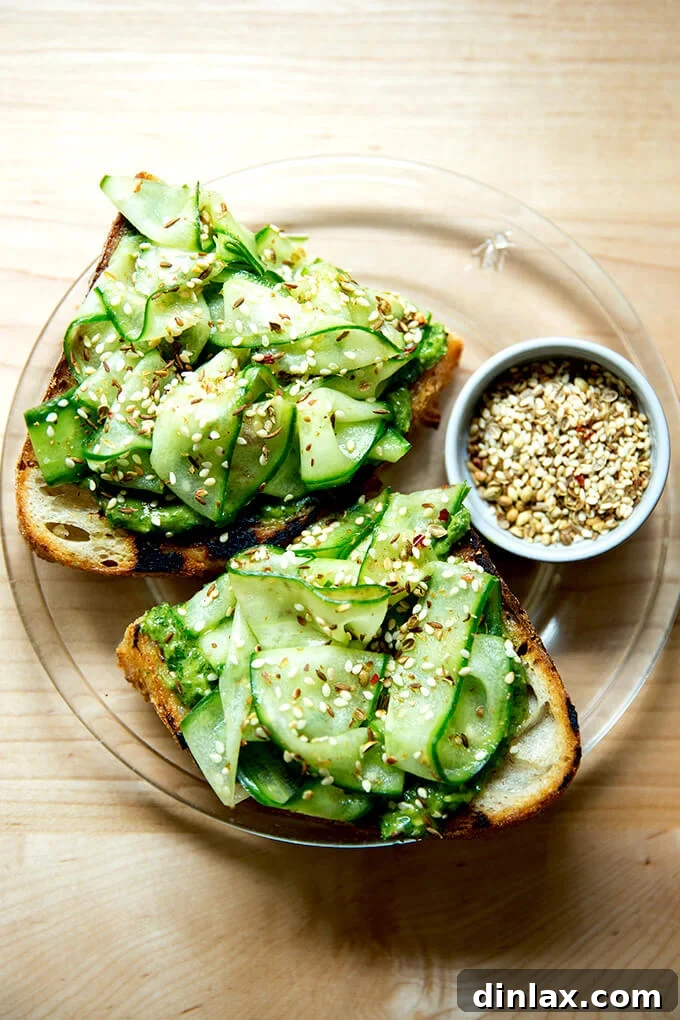 The Ultimate Herby Avocado Green Sauce 7 A plate featuring toast smeared with green sauce, topped with elegant sliced cucumbers and dukkah.