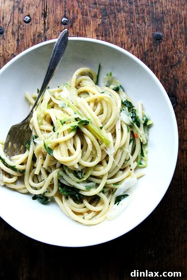 A close-up shot of one-pot bucatini pasta with vibrant green leeks and bright yellow lemon slices, emphasizing a fresh, simple, and flavorful pasta dish.