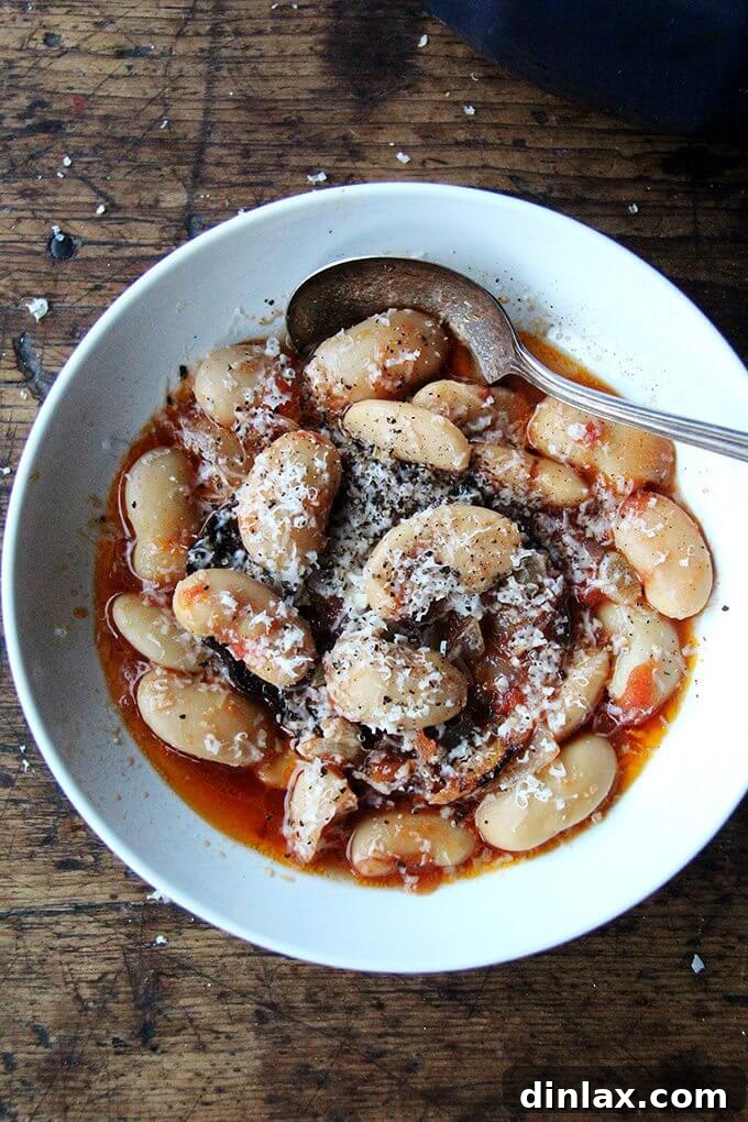 A close-up of baked corona beans, also known as gigante beans, slow-cooked with tomatoes and pancetta, illustrating a rustic and flavorful dish.