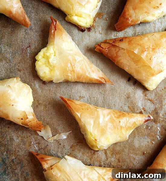 Just-baked tiropitas arranged on a sheet pan, showcasing their golden crust and crispy texture.