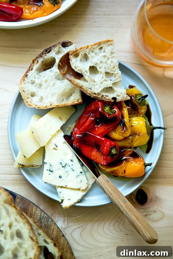 A rustic plate featuring roasted balsamic mini peppers, artisanal cheese, and slices of sourdough bread.