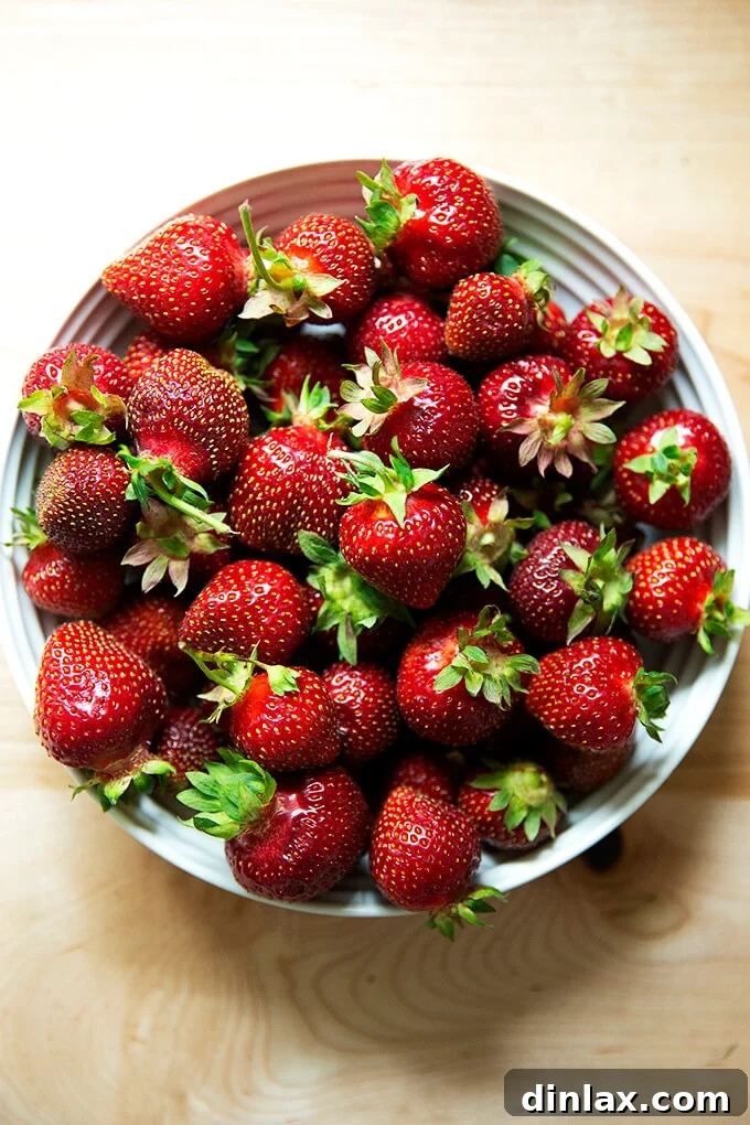A pristine white bowl filled to the brim with glistening, ripe strawberries, their vivid red hue radiating freshness and natural appeal.
