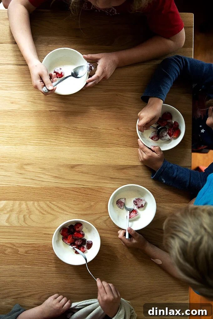 Four smiling children eagerly enjoying their individual bowls of fresh strawberries and cream, embodying the pure delight and simple pleasure this beloved dessert brings to all ages.
