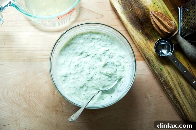 A clean, white bowl brimming with fresh, creamy cucumber-yogurt sauce, garnished with herbs, ready to cool down any spicy dish.