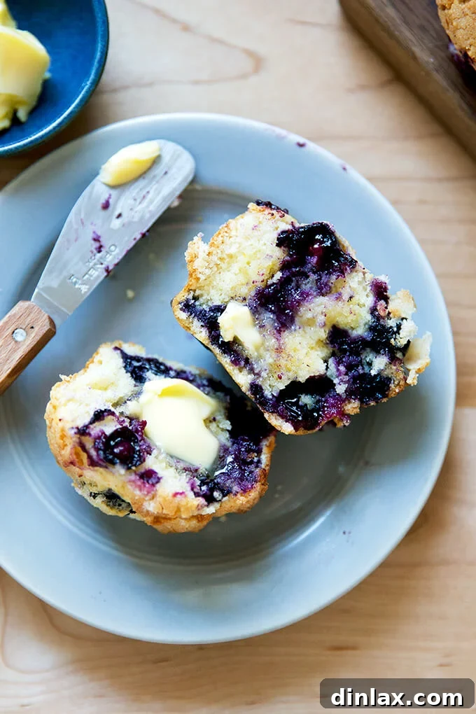 A halved blueberry muffin generously spread with butter, showing its moist interior.