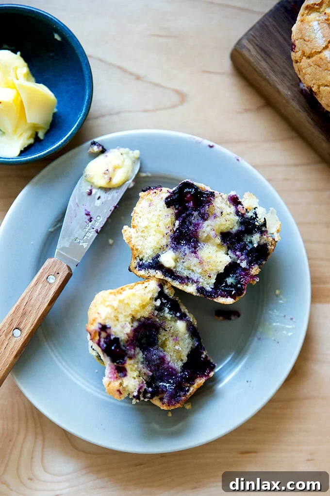 A close-up of a halved blueberry muffin with melted butter, steam gently rising.