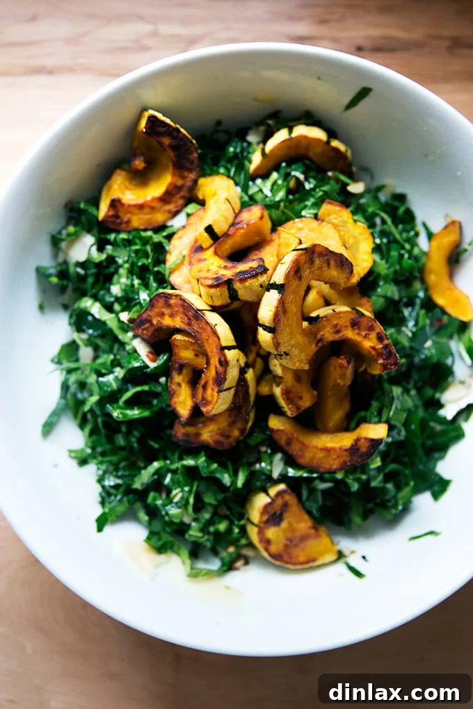 A bowl of fresh raw collard greens salad, now beautifully topped with warm, roasted delicata squash slices, preparing for the final toss.