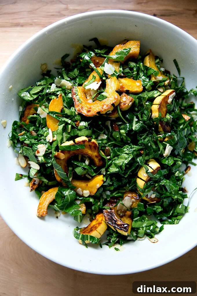 A large, inviting bowl filled with the fully tossed raw collard greens salad, featuring roasted delicata squash, toasted almonds, golden raisins, and Parmesan.