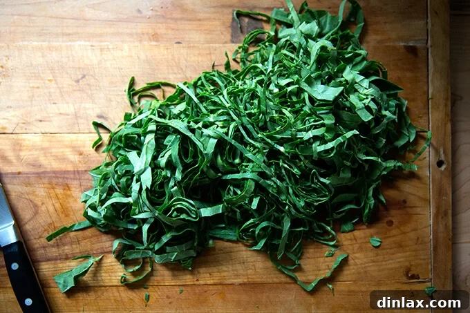Finely slivered collard greens, resembling delicate ribbons, neatly piled on a cutting board, ready for seasoning.