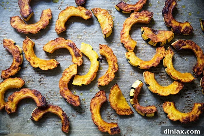 Golden-brown roasted delicata squash slices, caramelized and tender, spread evenly on a sheet pan after cooking.