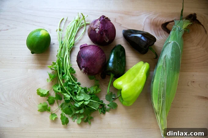 Fresh ingredients for salsa: lime, cilantro, red onions, poblano peppers, and corn kernels on a countertop.