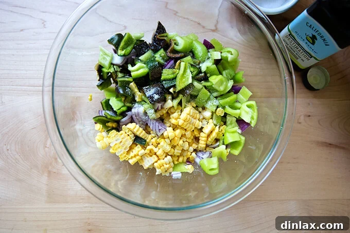 A bowl containing raw corn, poblano peppers, red onion, olive oil, and salt, pre-roasting.