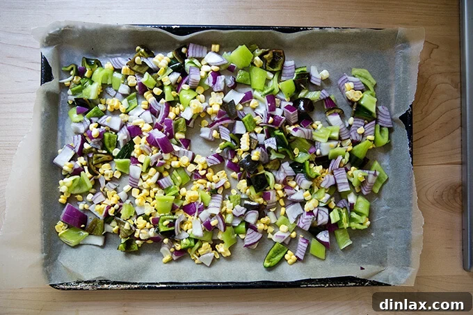 Chopped vegetables spread evenly on a sheet pan, seasoned and ready for the oven.