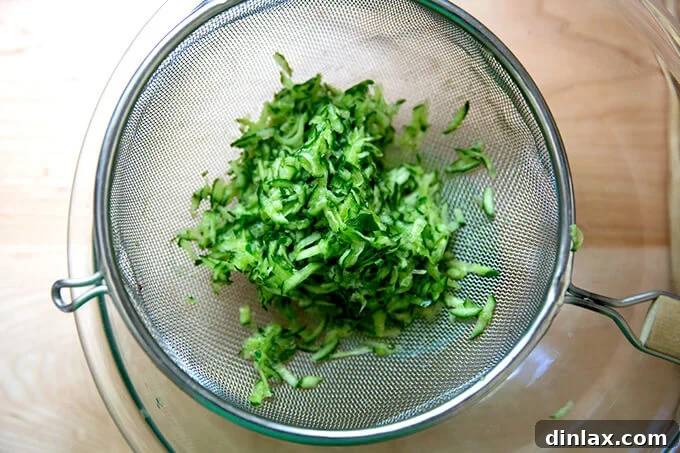 Grated cucumber draining thoroughly in a sieve, placed over a bowl to collect excess liquid.