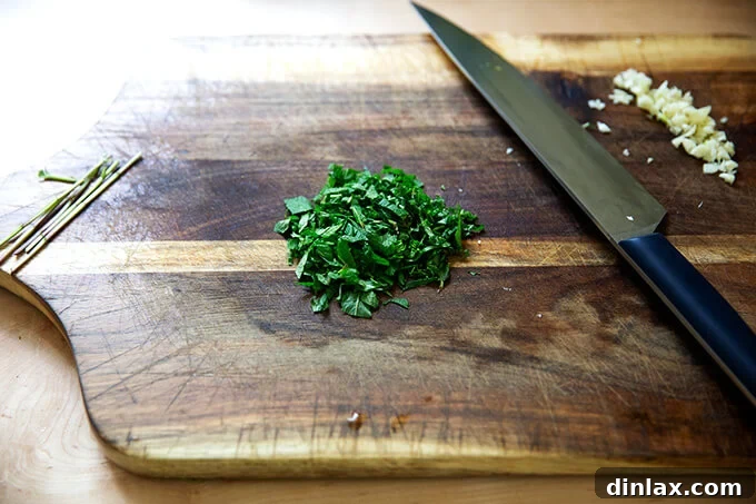 Fresh mint leaves and a clove of garlic finely chopped on a wooden cutting board, ready to be added to the tzatziki.