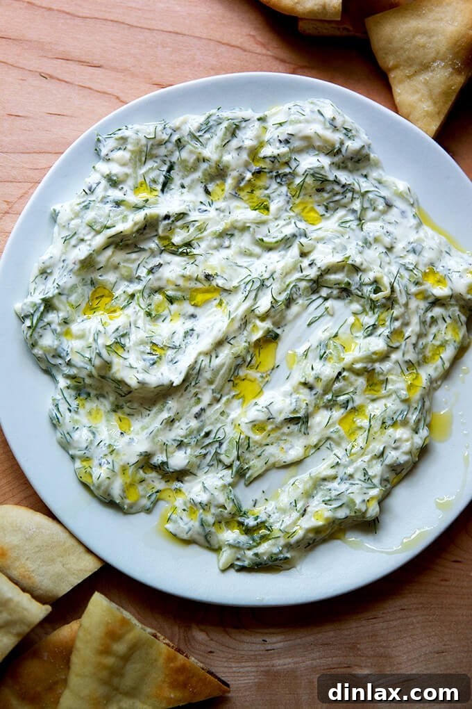 A generously portioned platter of tzatziki, beautifully adorned with a swirl of olive oil and fresh herbs, surrounded by perfectly toasted pita bread triangles.