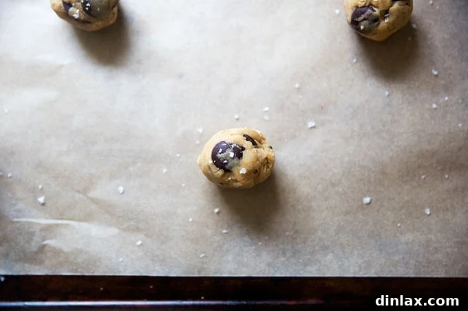 Decadent Gluten-Free Chocolate Chip Cookies 9 A gluten-free cookie dough ball on a sheet pan, adorned with a delicate sprinkling of flaky sea salt before baking.