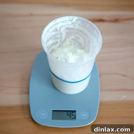 A hand adding flour to a sourdough starter in a jar on a digital scale.