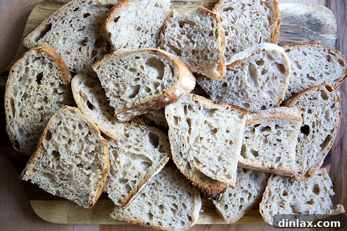 Simple Sourdough with a Hearty Whole Grain Touch 18 A rustic wooden board abundantly loaded with perfectly sliced pieces of high-hydration sourdough bread.
