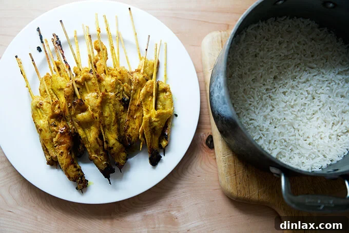 A rustic plate presents several skewers of cooked easy Thai chicken satay next to a pot of steamy, white coconut rice, highlighting the completed meal.