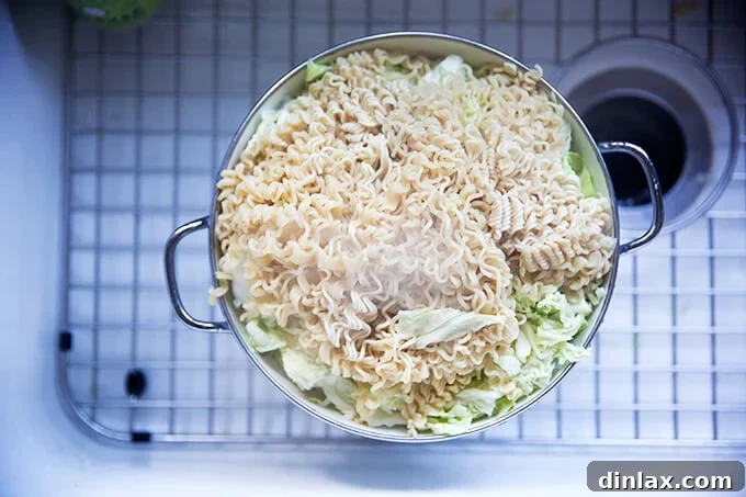 An overhead shot of a colander in a sink, holding finely shredded cabbage and freshly drained, par-cooked ramen noodles.