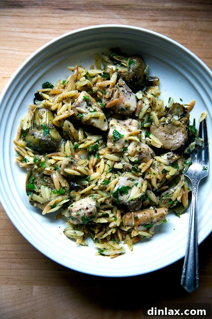 Zesty Lemon Artichoke Orzo Chicken Skillet 16 A single serving of one-pan lemon chicken orzo with artichoke hearts, garnished with fresh parsley on a white plate.