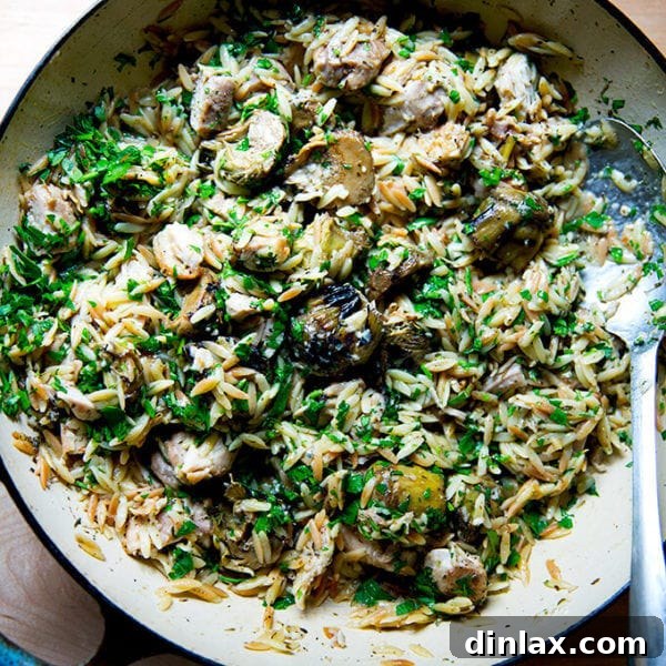 A close-up overhead shot of a skillet filled with one-pan lemon chicken orzo and artichoke hearts, garnished with fresh herbs.