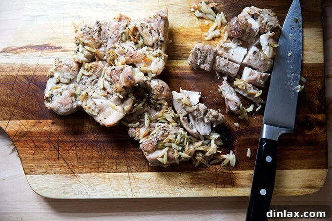 Zesty Lemon Artichoke Orzo Chicken Skillet 10 Cooked chicken thighs being cut into cubes on a wooden cutting board.