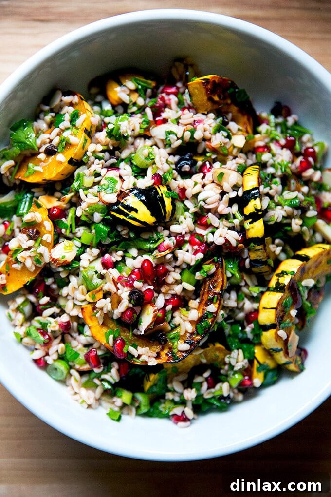 A vibrant white serving bowl filled with winter tabbouleh featuring roasted delicata squash slices, pomegranate arils, and fresh herbs.