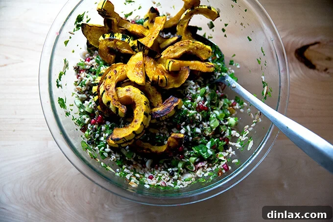 An overhead shot of a large glass bowl showcasing vibrant winter tabbouleh alongside golden-brown roasted delicata squash slices.
